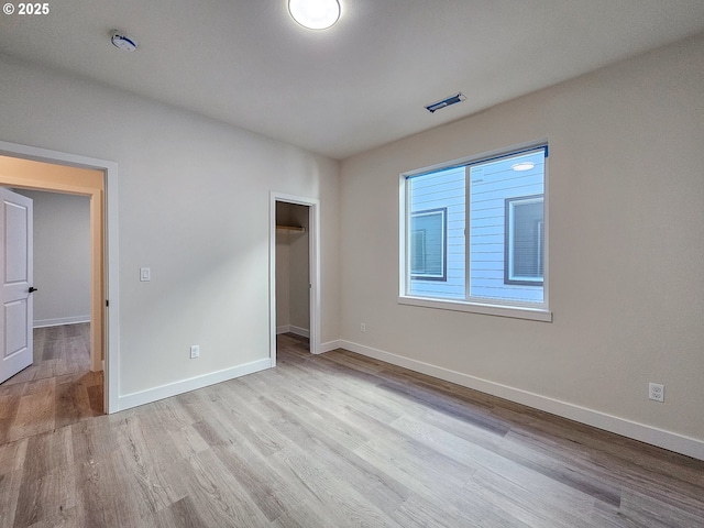 unfurnished bedroom with visible vents, a spacious closet, wood finished floors, and baseboards