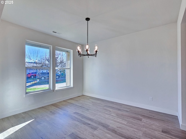 spare room featuring a chandelier, visible vents, baseboards, and wood finished floors