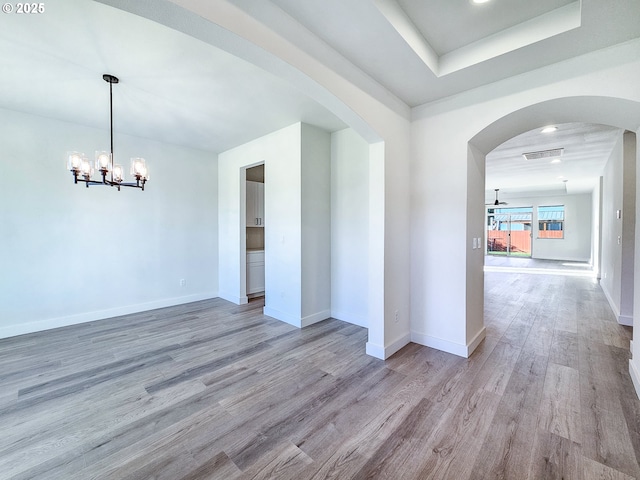 empty room with arched walkways, visible vents, light wood finished floors, and baseboards