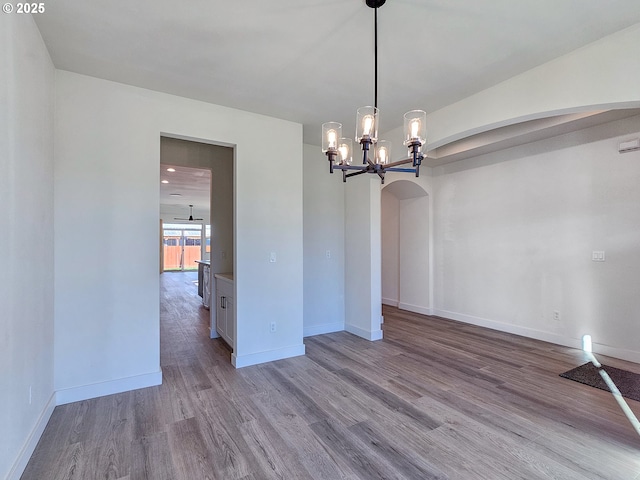 unfurnished dining area featuring arched walkways, a notable chandelier, baseboards, and wood finished floors