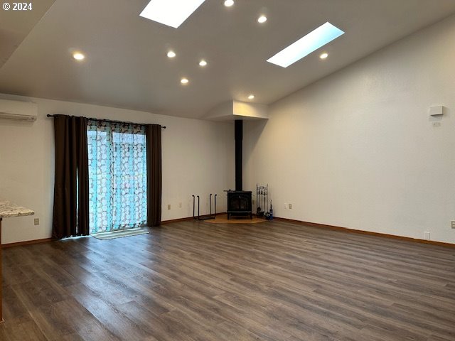 unfurnished living room with a wall unit AC, a wood stove, dark hardwood / wood-style flooring, and vaulted ceiling with skylight