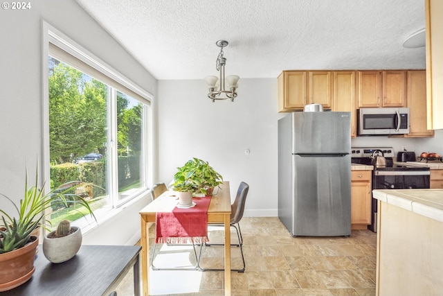 kitchen with pendant lighting, appliances with stainless steel finishes, a notable chandelier, a textured ceiling, and tile countertops