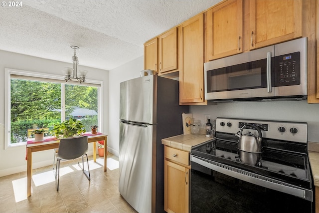 kitchen featuring appliances with stainless steel finishes, a notable chandelier, tile counters, a textured ceiling, and decorative light fixtures