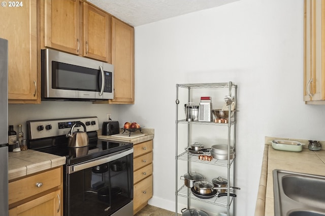 kitchen featuring stainless steel appliances, sink, tile counters, and a textured ceiling