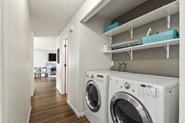 clothes washing area with a fireplace, a textured ceiling, washing machine and clothes dryer, and dark hardwood / wood-style flooring