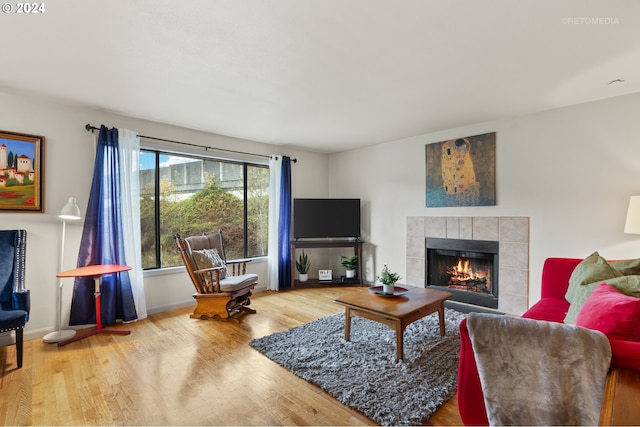 living room with a tile fireplace, baseboards, and wood finished floors