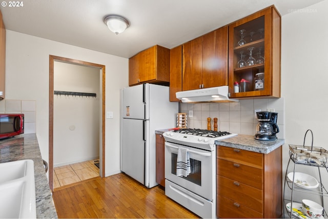 kitchen with tasteful backsplash, brown cabinetry, white appliances, light wood-style flooring, and under cabinet range hood