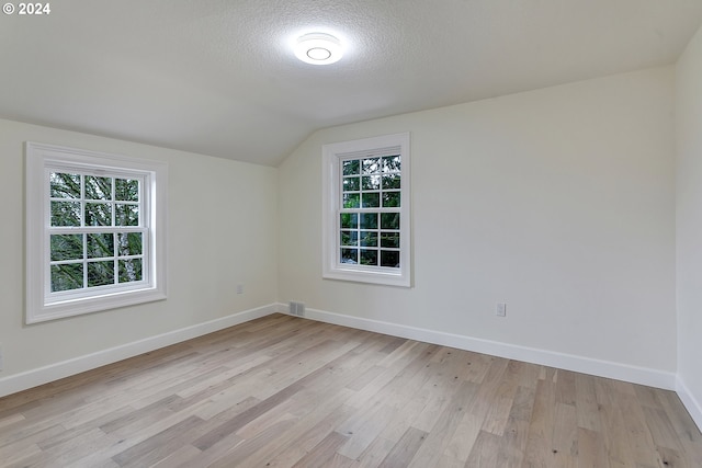 empty room featuring light hardwood / wood-style floors, vaulted ceiling, and a healthy amount of sunlight