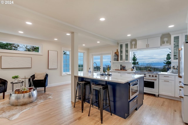 kitchen with white cabinets, decorative backsplash, light wood-type flooring, an island with sink, and appliances with stainless steel finishes