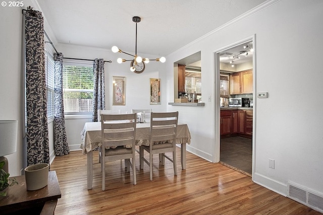 dining area with crown molding, a chandelier, and light wood-type flooring