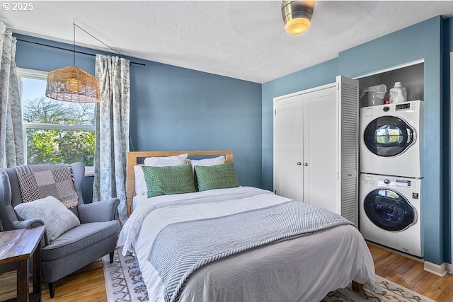 bedroom with a textured ceiling, ceiling fan, hardwood / wood-style floors, and stacked washer / drying machine