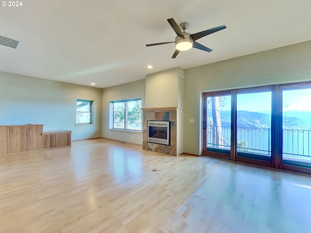 unfurnished living room with a mountain view, ceiling fan, light wood-type flooring, and a tile fireplace