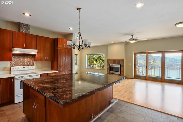 kitchen featuring white range with electric stovetop, backsplash, pendant lighting, a fireplace, and ceiling fan with notable chandelier