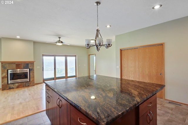 kitchen with a center island, hanging light fixtures, a tiled fireplace, light tile patterned flooring, and ceiling fan with notable chandelier