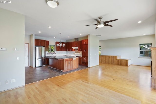 kitchen featuring a center island, dark wood-type flooring, hanging light fixtures, a wealth of natural light, and stainless steel refrigerator