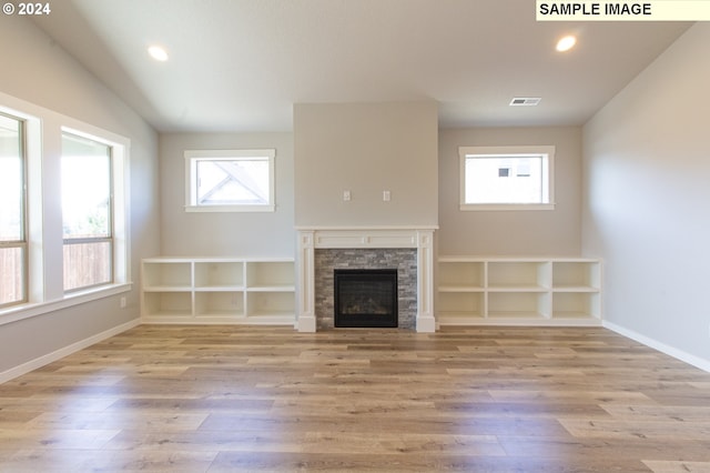 unfurnished living room featuring a stone fireplace, plenty of natural light, and light hardwood / wood-style floors