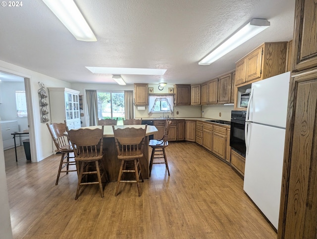 kitchen with a breakfast bar area, wood-type flooring, black oven, white fridge, and a kitchen island