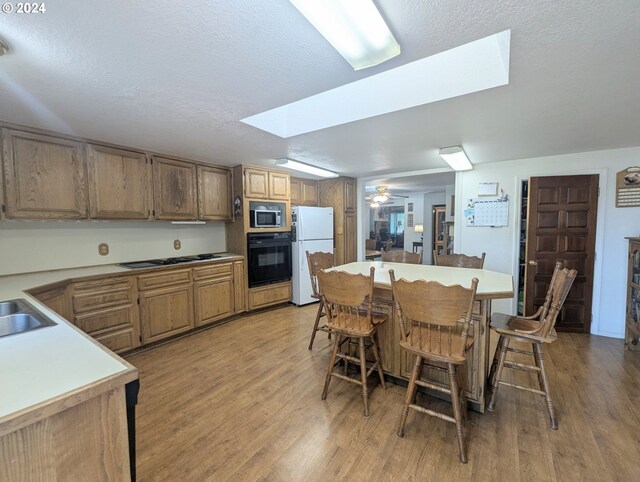 kitchen featuring white fridge, stainless steel microwave, black oven, light wood-type flooring, and ceiling fan