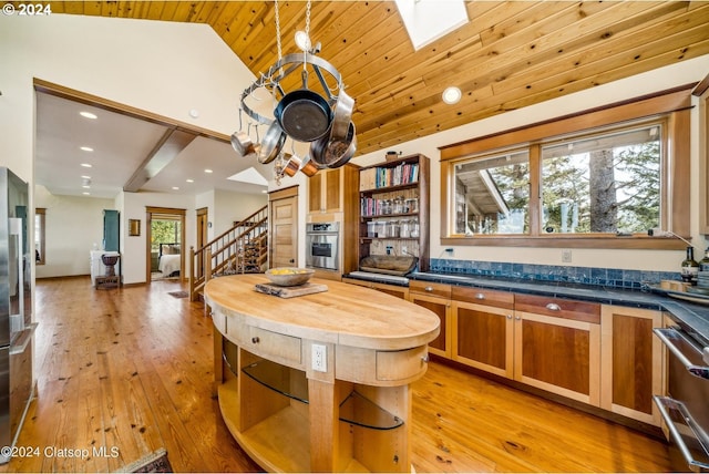 kitchen with stainless steel oven, vaulted ceiling with skylight, wooden ceiling, and light hardwood / wood-style floors