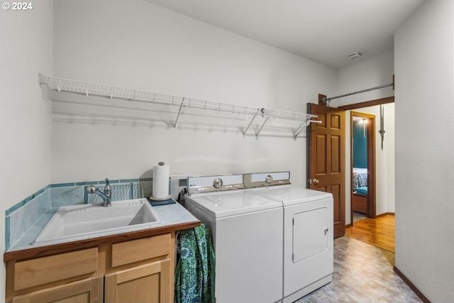 clothes washing area with light hardwood / wood-style flooring, separate washer and dryer, cabinets, and sink