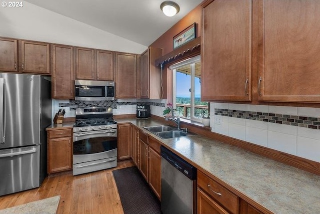 kitchen featuring lofted ceiling, sink, light wood-type flooring, appliances with stainless steel finishes, and backsplash