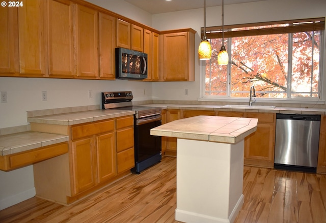 kitchen with tile countertops, sink, light hardwood / wood-style floors, and appliances with stainless steel finishes