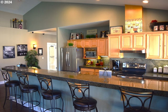 kitchen featuring a kitchen bar, appliances with stainless steel finishes, tasteful backsplash, and lofted ceiling