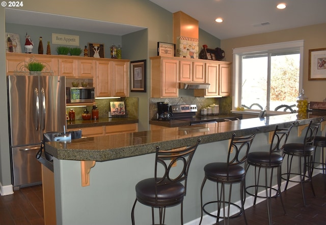 kitchen with dark wood-type flooring, stainless steel appliances, vaulted ceiling, a breakfast bar area, and decorative backsplash