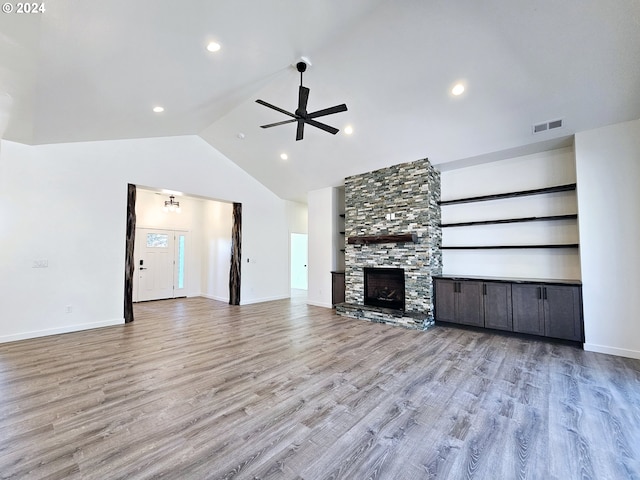 unfurnished living room featuring ceiling fan, light wood-type flooring, high vaulted ceiling, and a stone fireplace