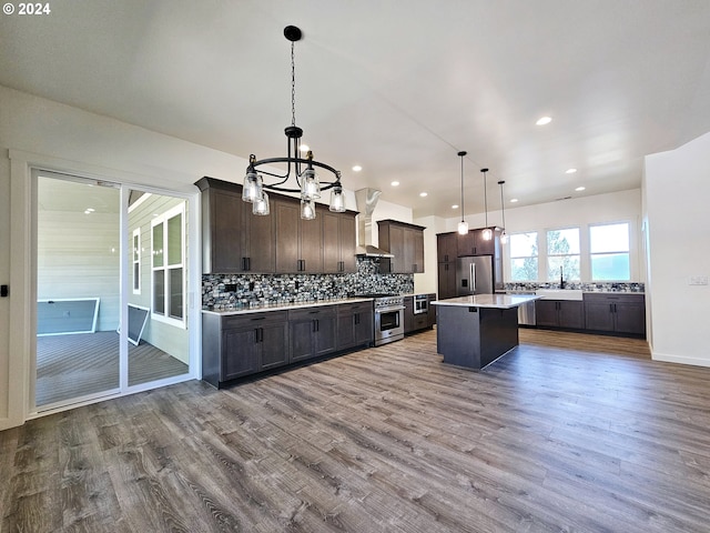 kitchen with high end appliances, wood-type flooring, a kitchen island, dark brown cabinetry, and decorative light fixtures