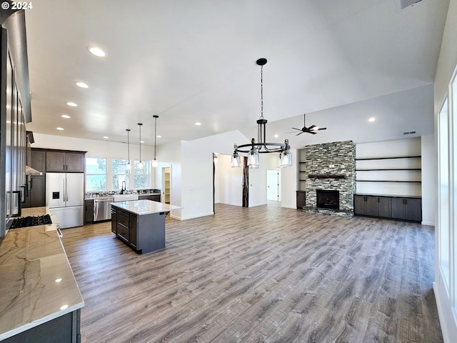 kitchen with dark brown cabinets, appliances with stainless steel finishes, light hardwood / wood-style floors, light stone counters, and a center island