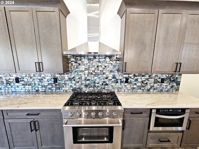 kitchen with backsplash, stainless steel appliances, light stone counters, and wall chimney exhaust hood