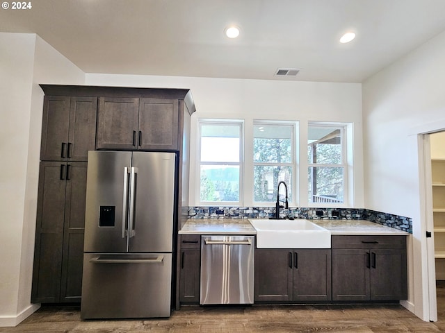 kitchen featuring stainless steel appliances, dark brown cabinets, tasteful backsplash, sink, and wood-type flooring