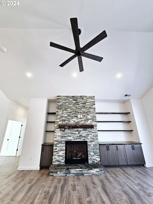 unfurnished living room featuring ceiling fan, light wood-type flooring, built in shelves, and a stone fireplace