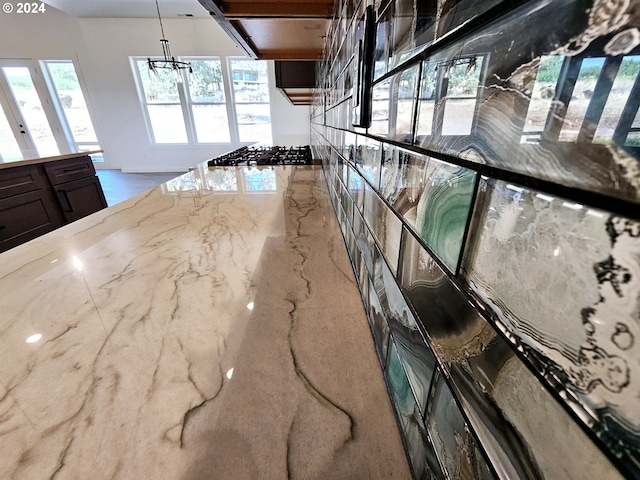 kitchen with a notable chandelier, stainless steel gas cooktop, light stone counters, and decorative light fixtures