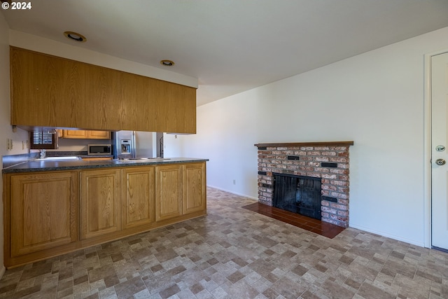 kitchen with sink, kitchen peninsula, stainless steel appliances, and a brick fireplace