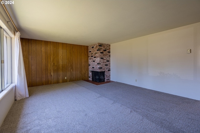 unfurnished living room featuring a fireplace, carpet flooring, and wood walls