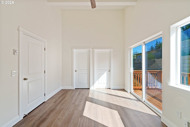 interior space with beamed ceiling, a high ceiling, and light wood-type flooring