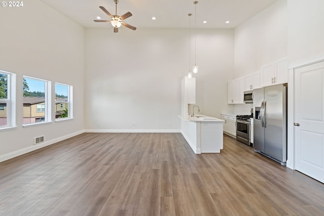 kitchen with kitchen peninsula, appliances with stainless steel finishes, pendant lighting, white cabinets, and a high ceiling