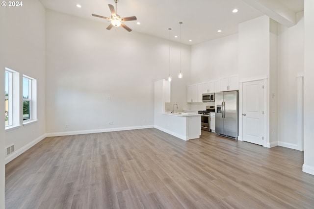 unfurnished living room with ceiling fan, light hardwood / wood-style flooring, a high ceiling, and sink