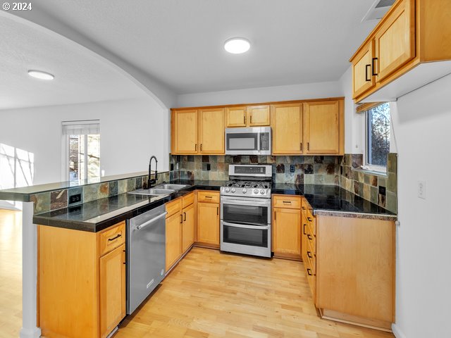 kitchen with sink, kitchen peninsula, light hardwood / wood-style floors, decorative backsplash, and appliances with stainless steel finishes