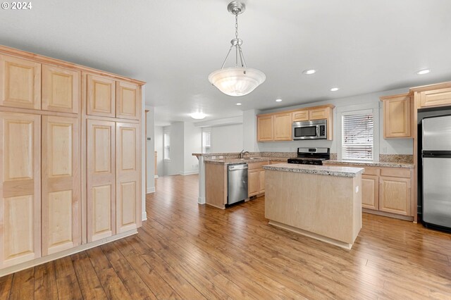 kitchen featuring light brown cabinets, light hardwood / wood-style floors, light stone countertops, a center island, and stainless steel appliances