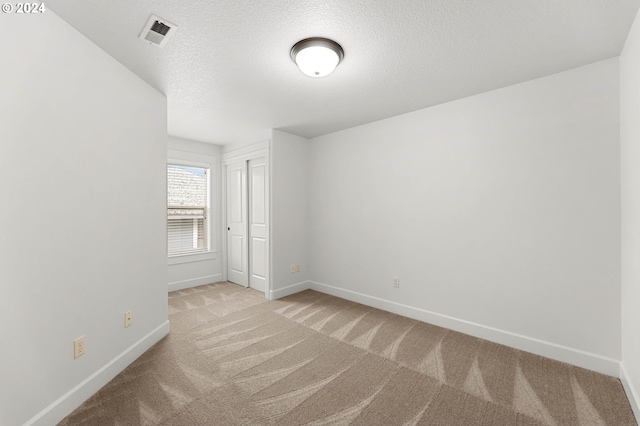 empty room with light colored carpet and a textured ceiling