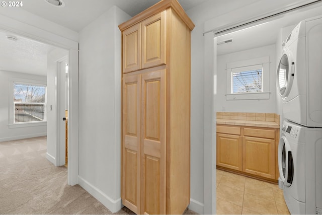 laundry room featuring a wealth of natural light, stacked washer and dryer, cabinets, and light carpet