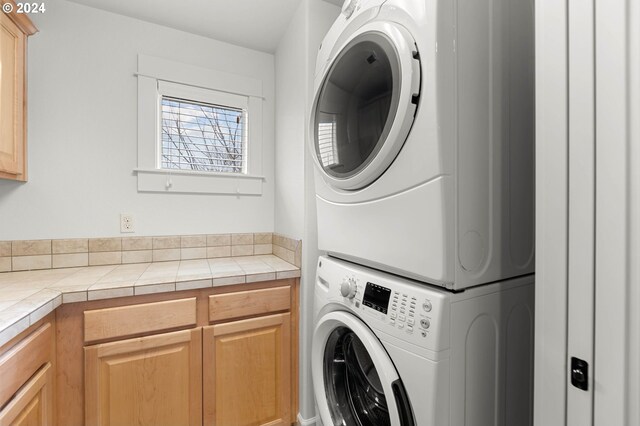 laundry room with stacked washer and clothes dryer and cabinets