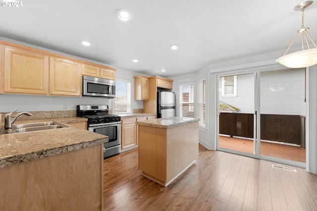 kitchen with stainless steel appliances, light hardwood / wood-style floors, sink, light brown cabinets, and hanging light fixtures