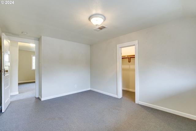 unfurnished bedroom with dark colored carpet, a spacious closet, and a closet