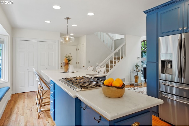 kitchen featuring blue cabinetry, a center island, light hardwood / wood-style flooring, pendant lighting, and appliances with stainless steel finishes