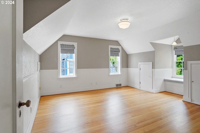 additional living space with a healthy amount of sunlight, vaulted ceiling, and light wood-type flooring