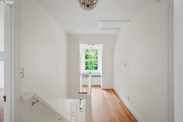 corridor with a textured ceiling, light hardwood / wood-style flooring, and vaulted ceiling